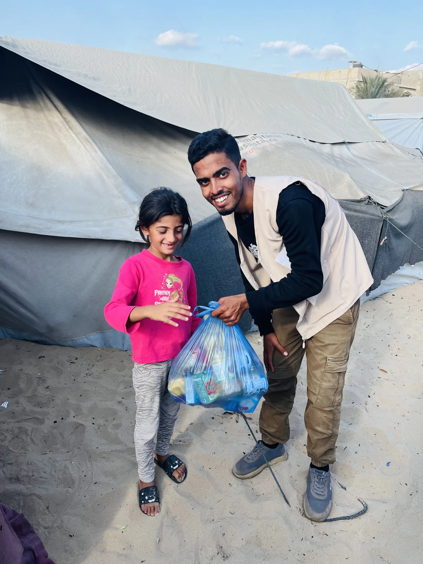 A humanitarian aid bag being handed to a child beside a tent