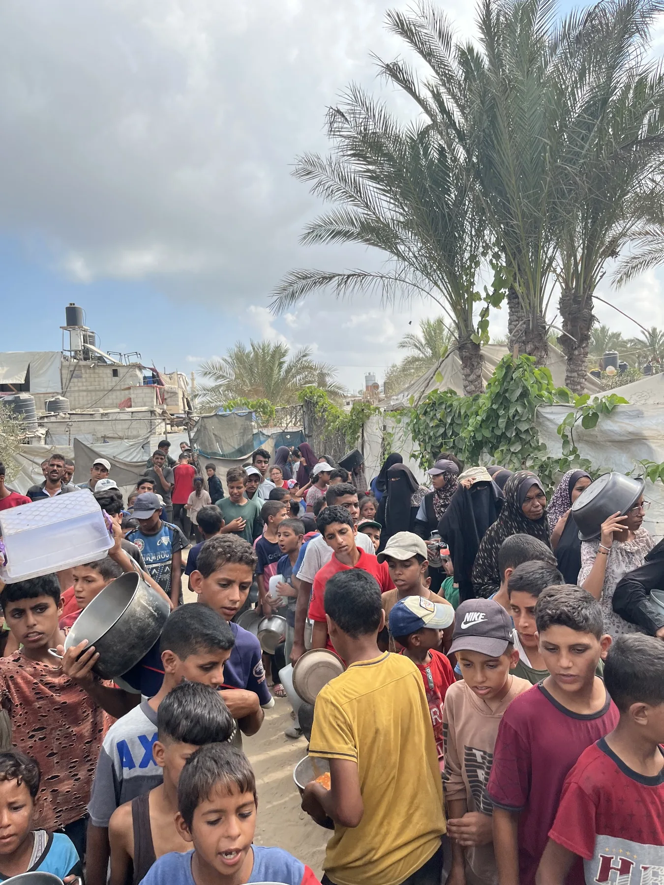 Families gathered with containers in a displacement community