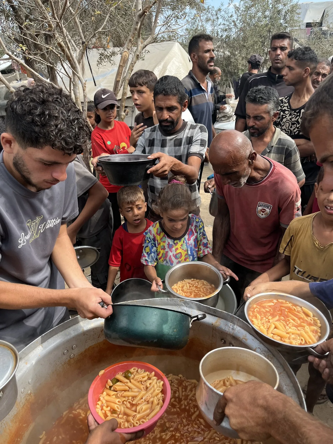 Families receiving prepared meals from a large cooking pot